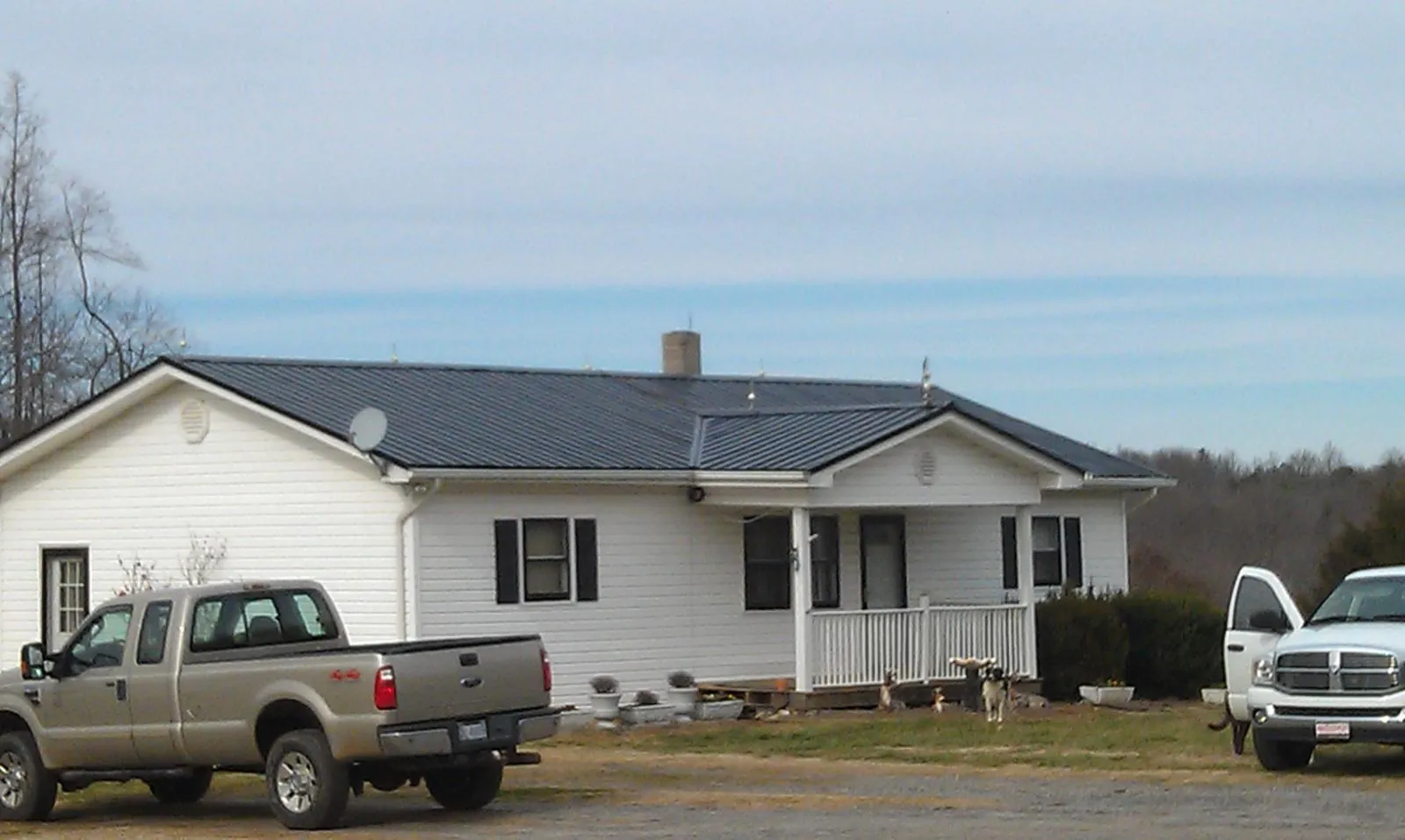 Finished dark metal roof on a white ranch home with work trucks parked in Salem
